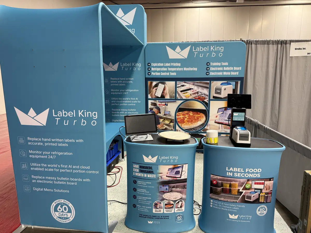 Close-up of Label King Turbo demo counters at Pizza Expo with a portion scale, tablet displays, a label printer, and label rolls